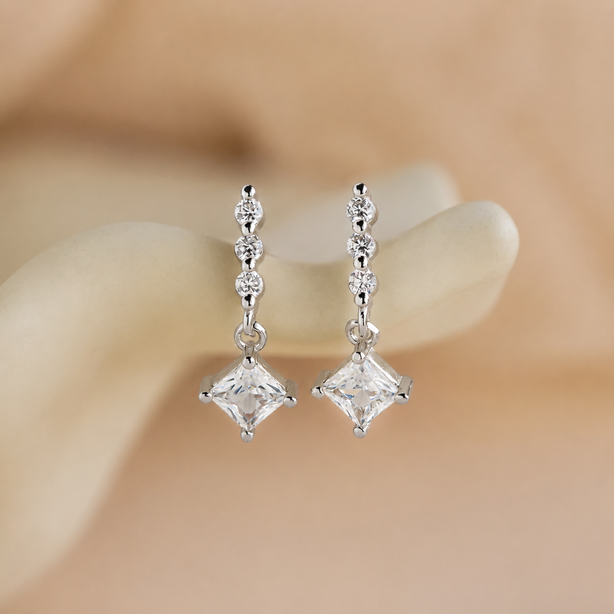 Silver earrings with clear gemstones on a blurred beige background